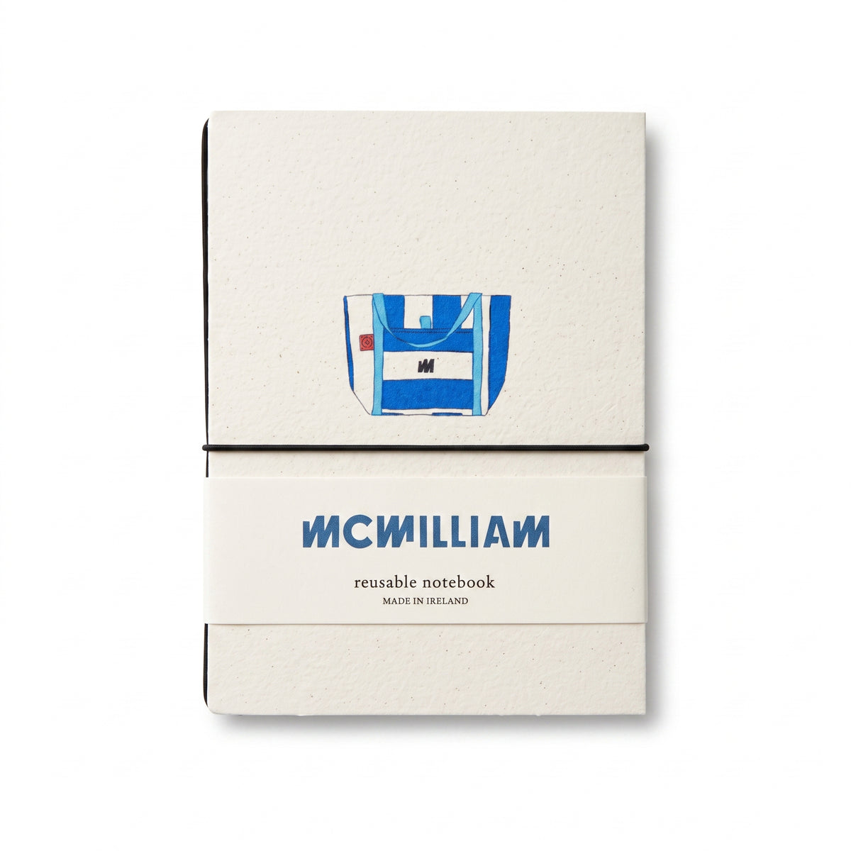 McWilliam reusable notebook in a cream-colored kraft paper cover with a blue and white graphic illustration of a backpack on the upper half and the brand name 'MCMILLIAM' printed in blue on the lower half, wrapped in a black elastic band.